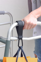 Load image into Gallery viewer, bag hook in use attached to a walker with a bag hanging off of it.

