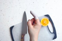 Charger l&#39;image dans la galerie, a hand with one finger wearing a finger cot with a knife and a cutting board on the background
