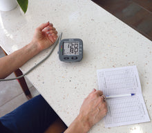 Charger l'image dans la galerie, blood pressure monitor in action taking a reading, patients log book on the side